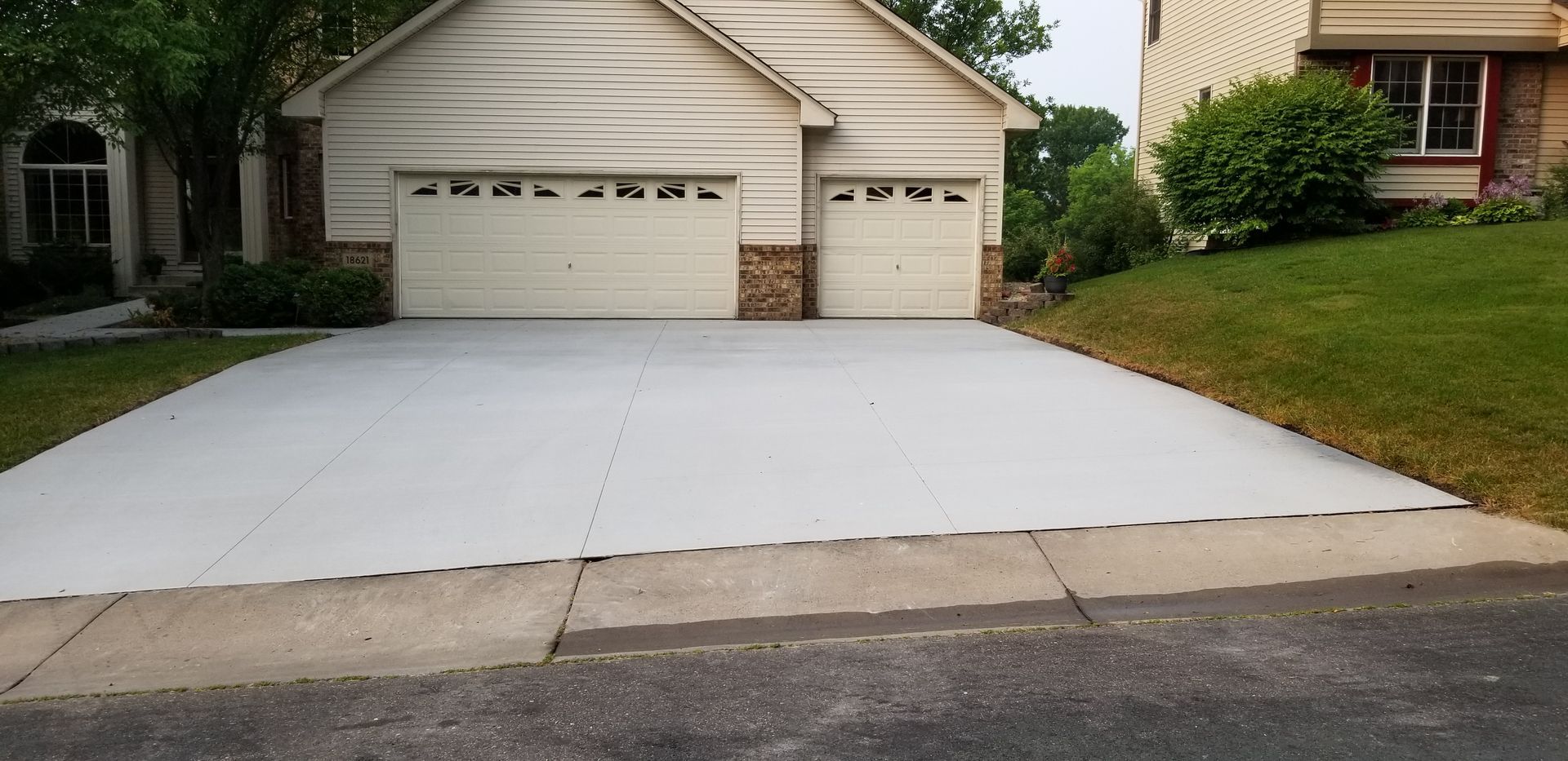 A house with a light-colored exterior and garage doors, a concrete driveway, and grassy areas.
