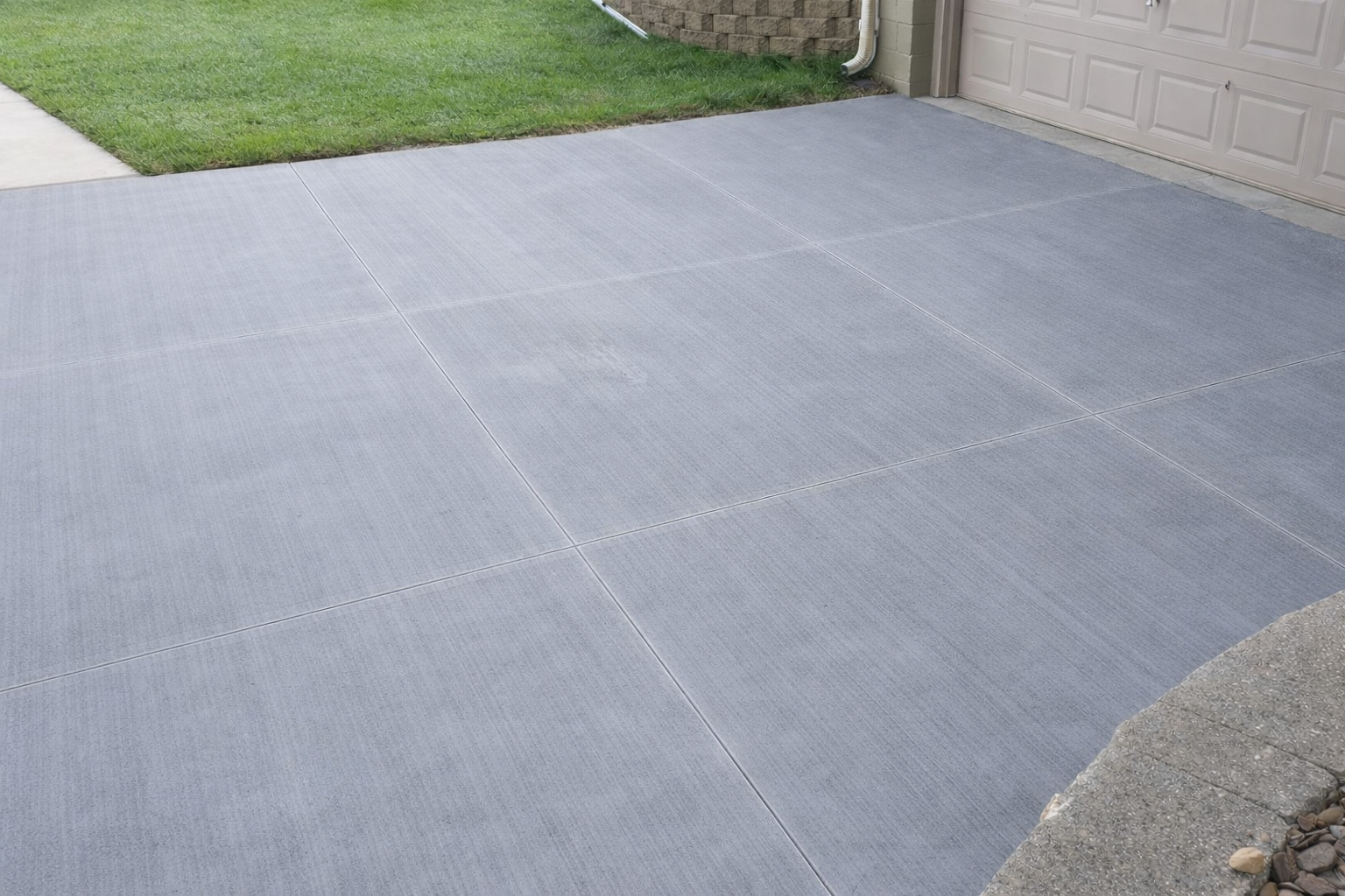 Gray interlocking patio tiles next to green grass and a beige brick wall.