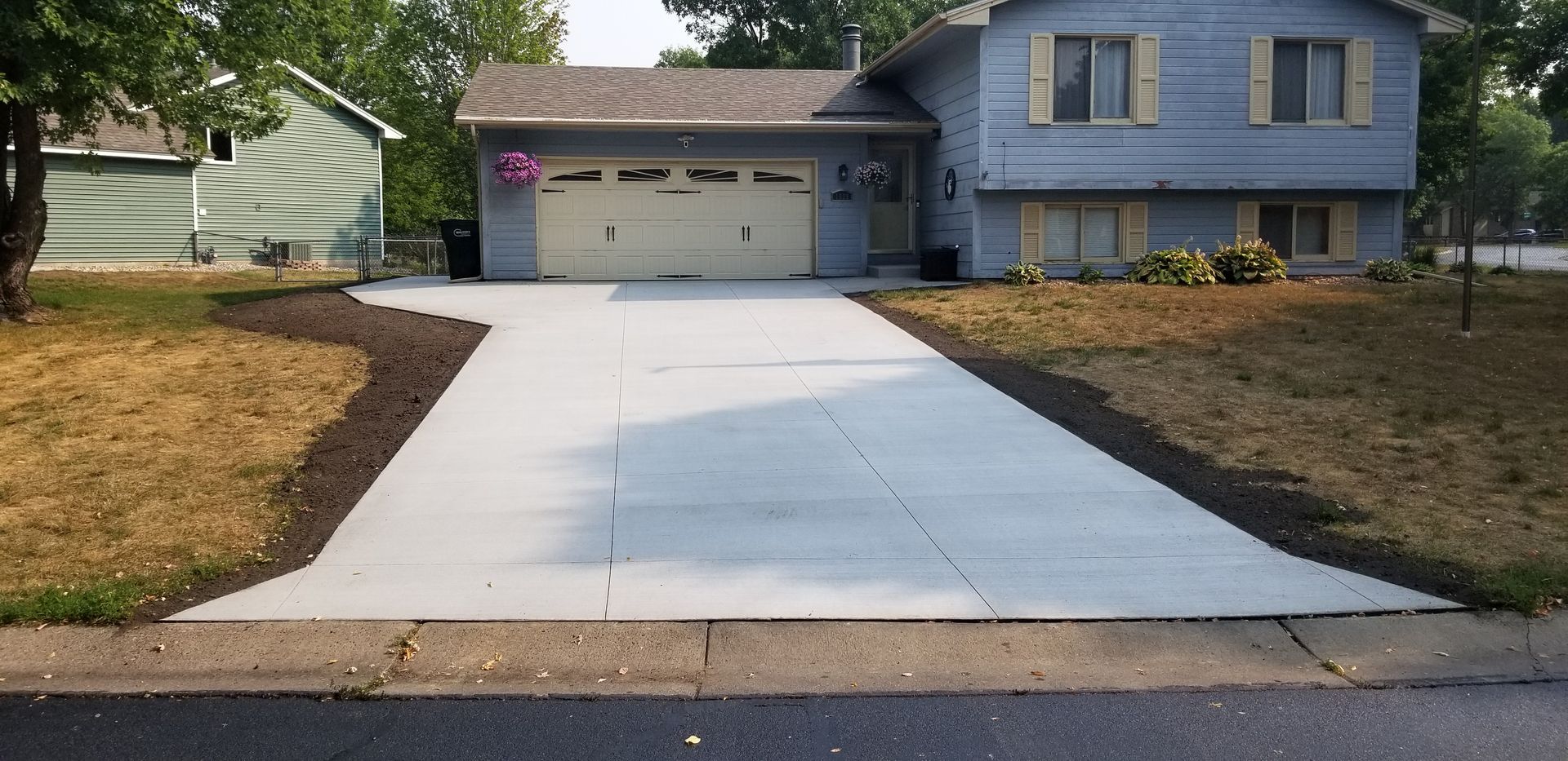 House with light blue siding, light-colored garage door, and newly poured concrete driveway. Brown mulch borders the driveway.