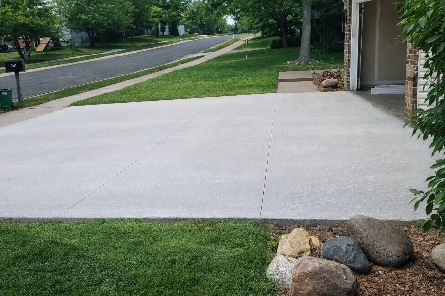 Driveway and lawn of a house next to a street; a few decorative rocks are in the yard.