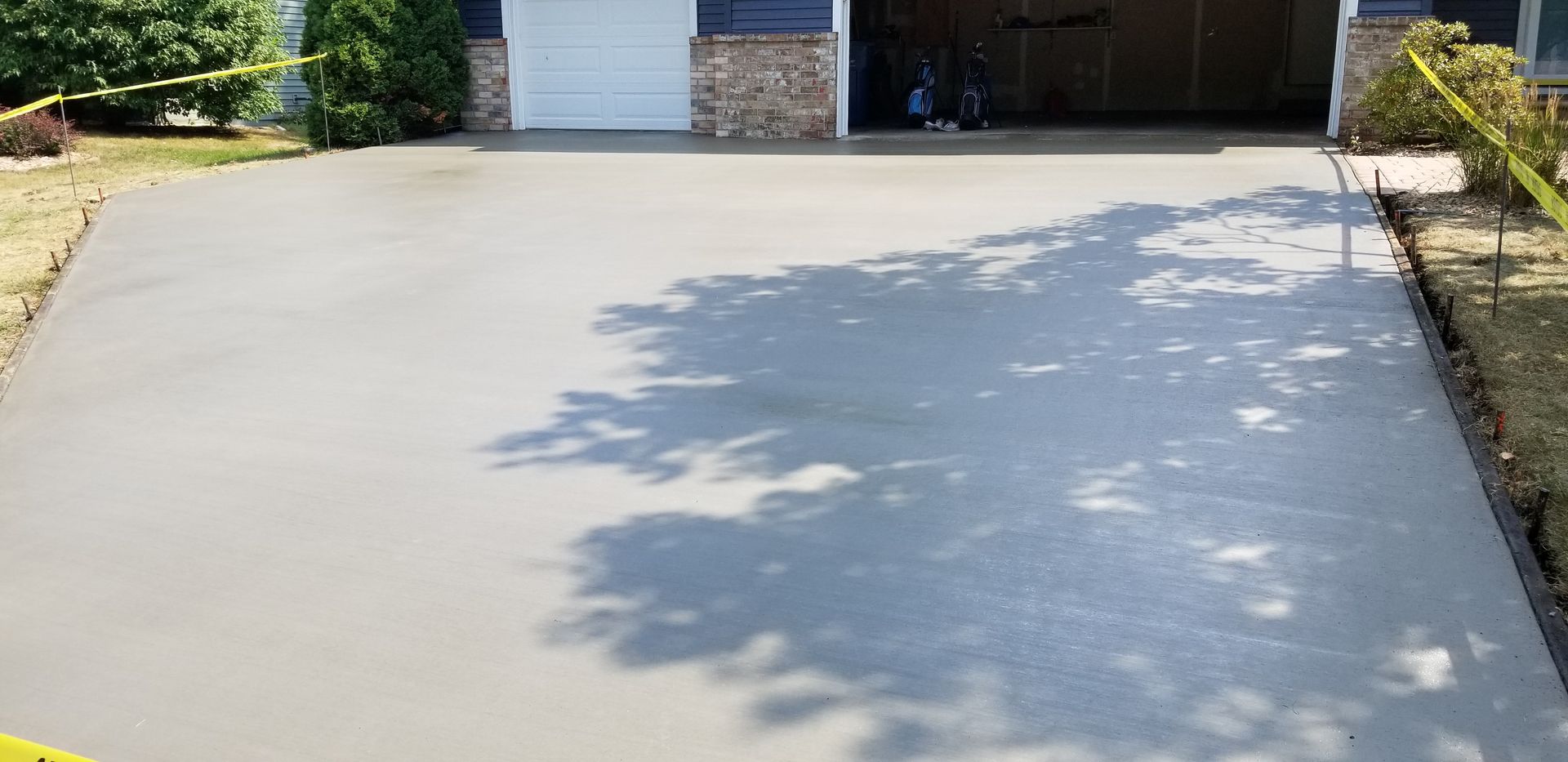 Newly poured concrete driveway with shadows cast by trees, garage in background.