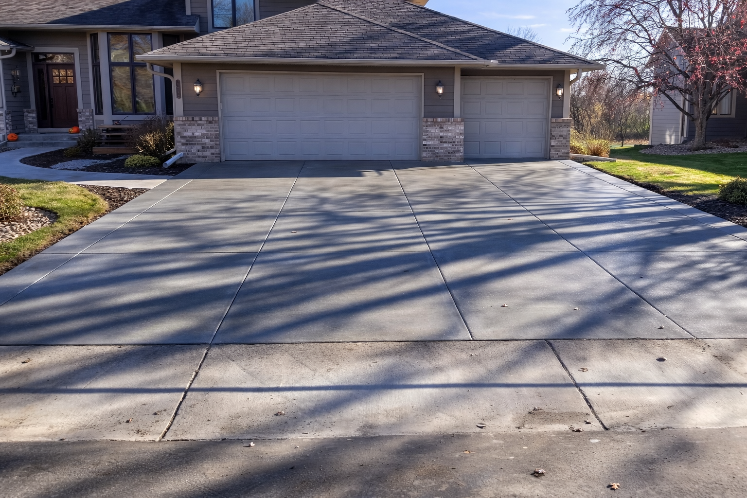 Concrete driveway leading to a two-car garage of a house. Sunlight casts shadows across the concrete.