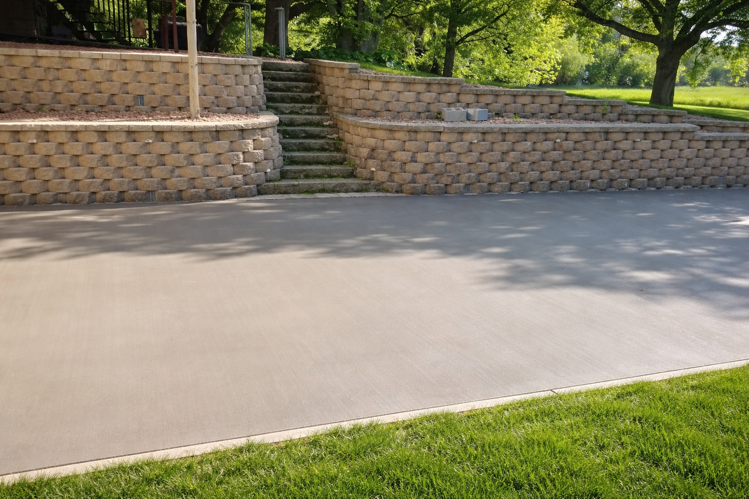 Concrete patio in front of tiered retaining wall with steps, next to green grass.