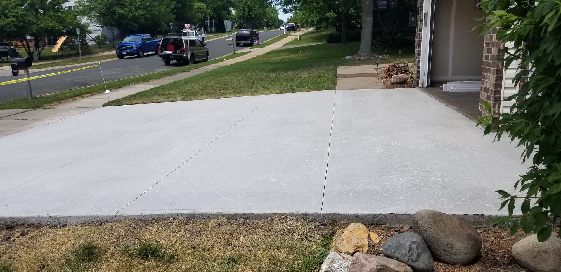 A newly poured concrete driveway leads to a house with vehicles driving on a street in the background.
