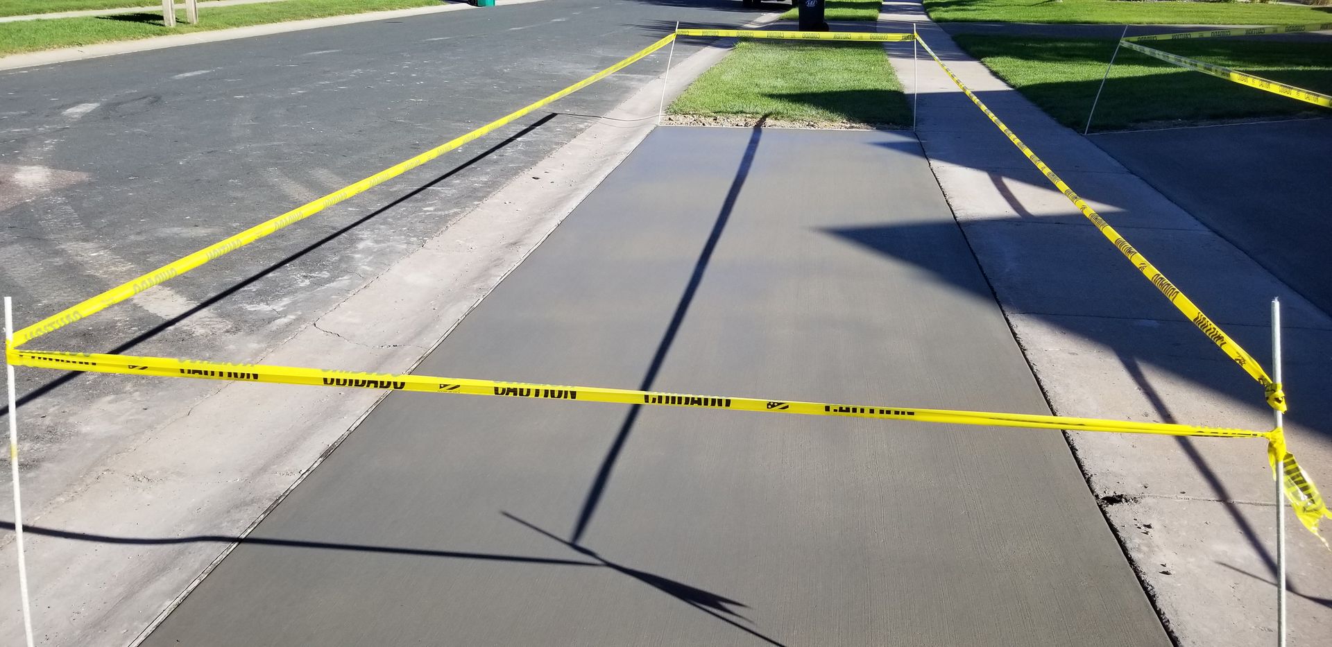 Freshly poured concrete driveway section, surrounded by yellow caution tape.