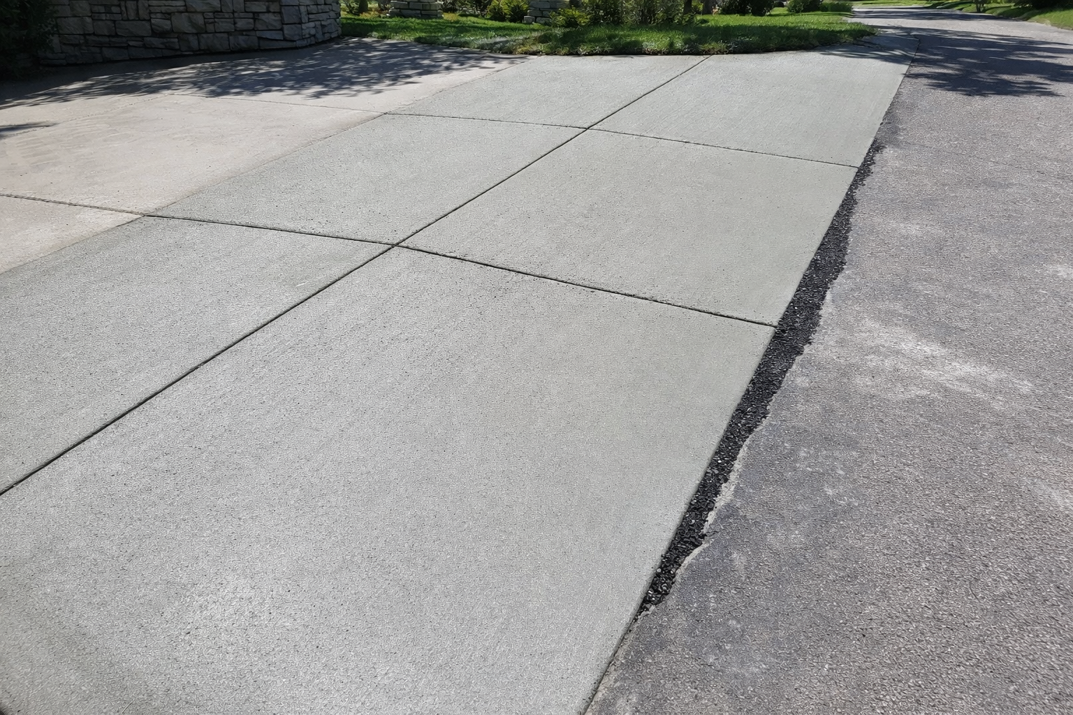 Gray concrete driveway with expansion joints and asphalt edges.