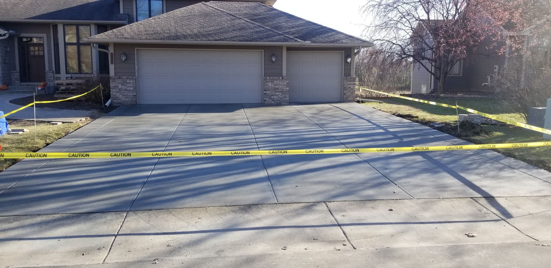 House with a driveway marked with caution tape. Two-car garage, gray concrete driveway, and grassy areas on either side.