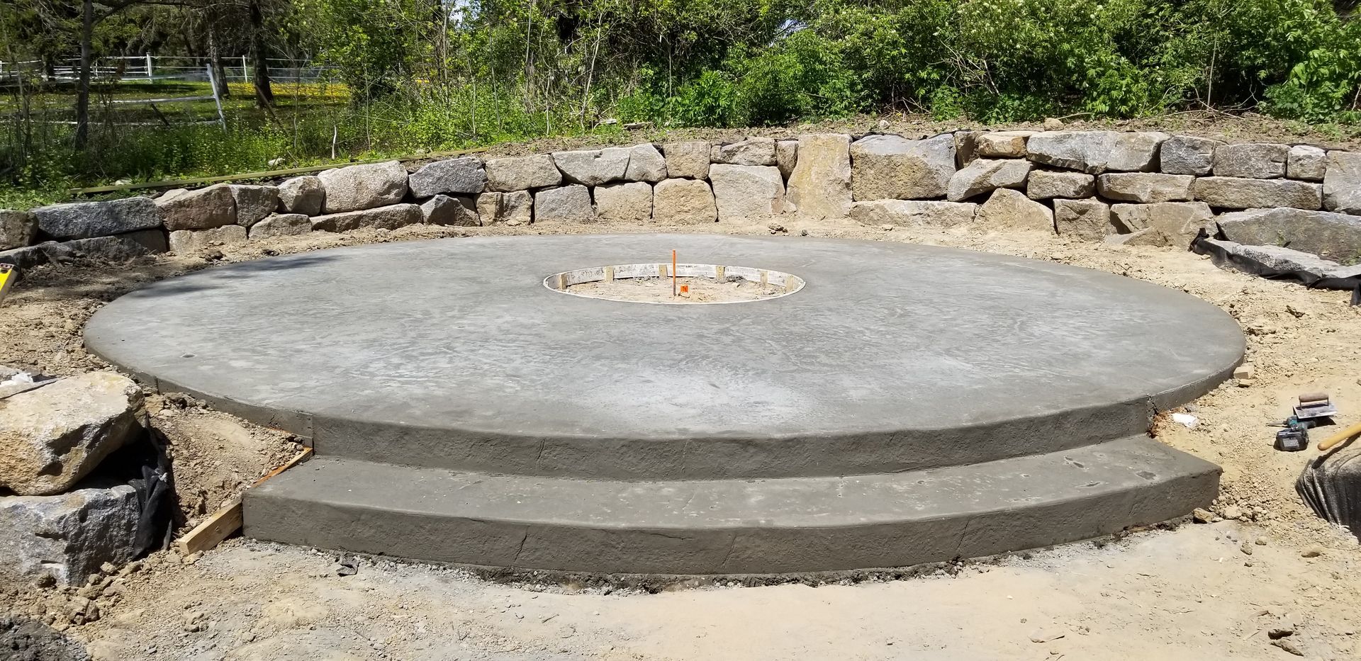 Concrete fire pit base with two steps, under construction outdoors.