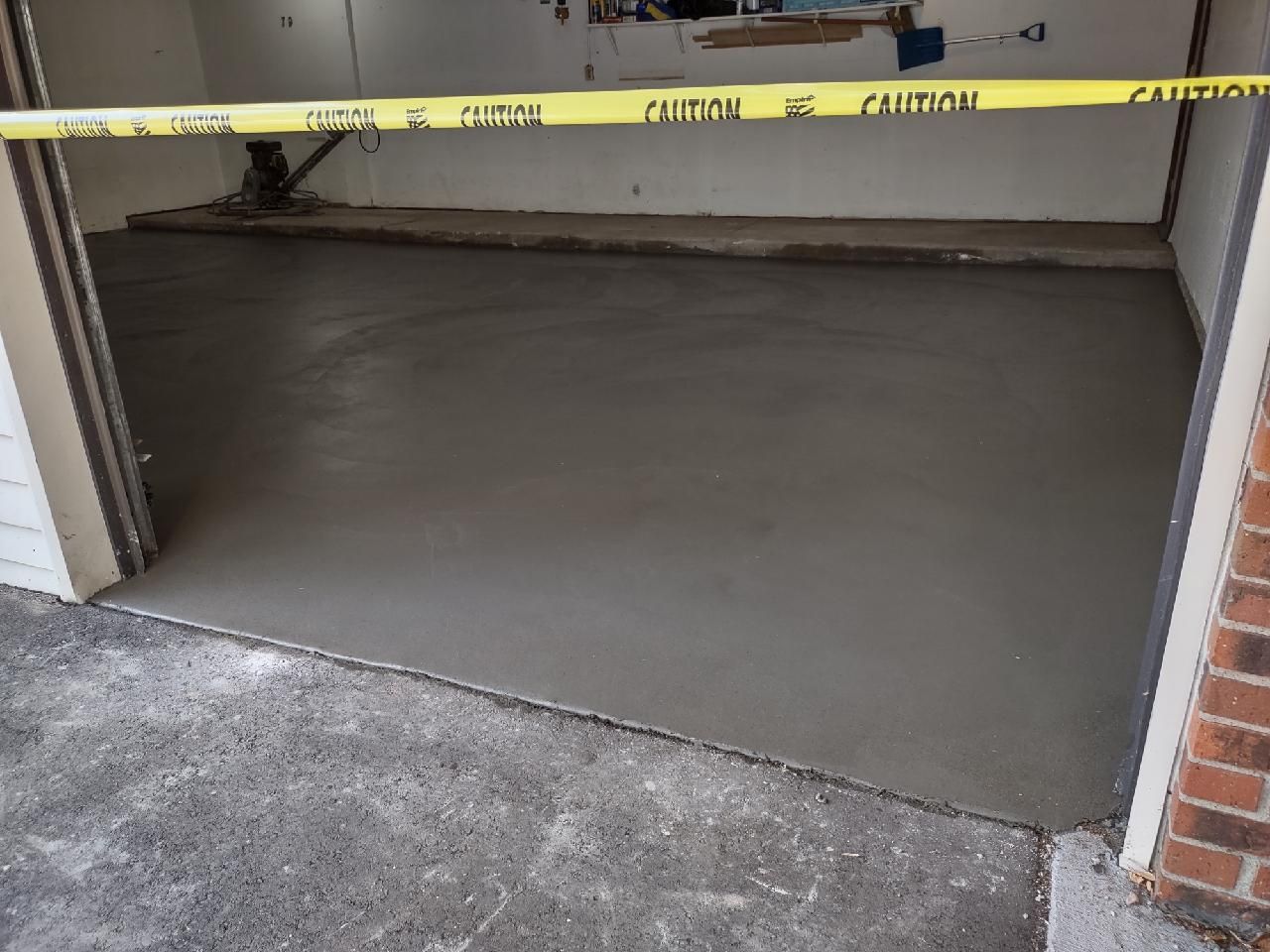 Newly poured concrete garage floor, blocked by yellow caution tape.