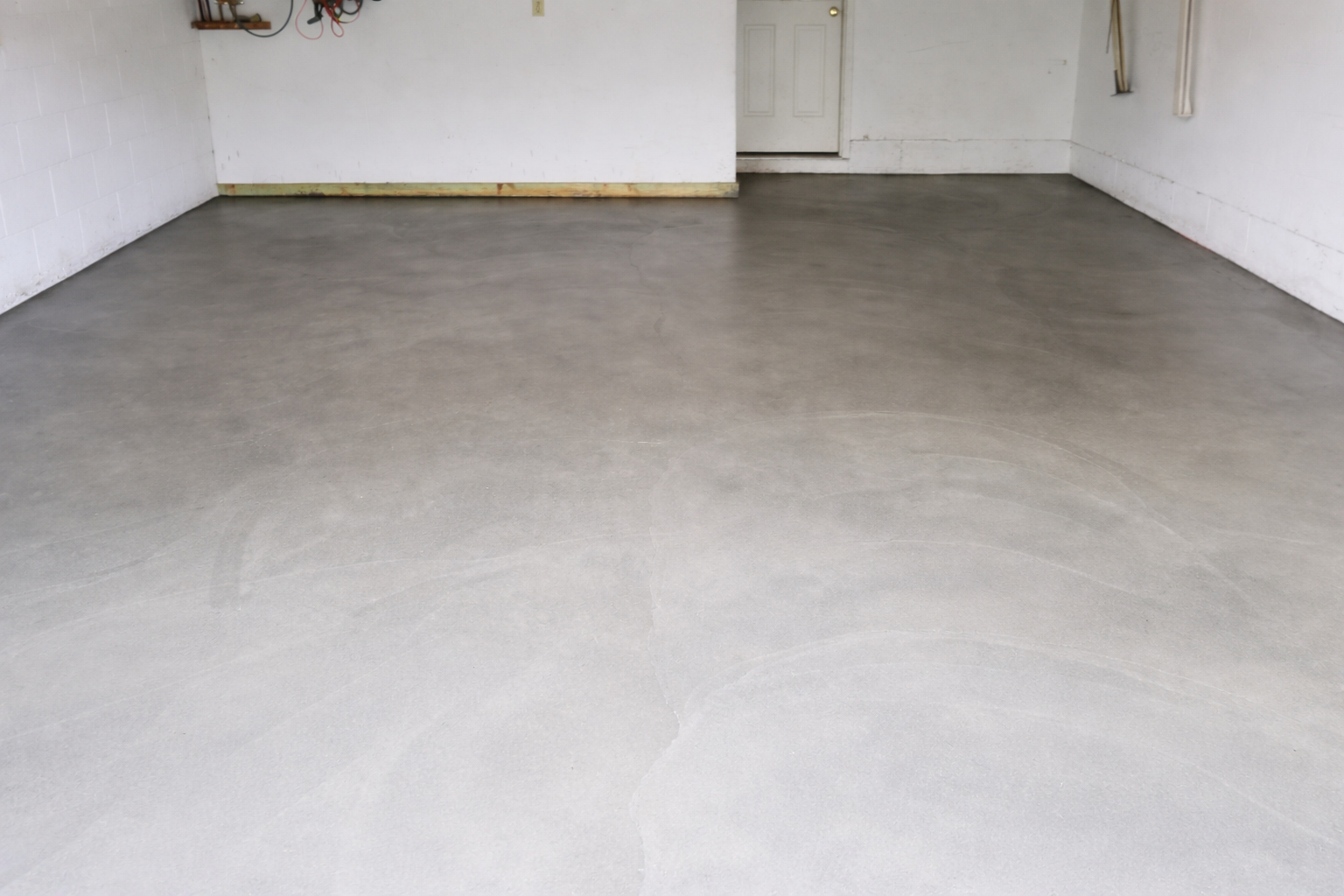 Empty garage interior with a smooth, gray concrete floor. White walls and a doorway are in the background.