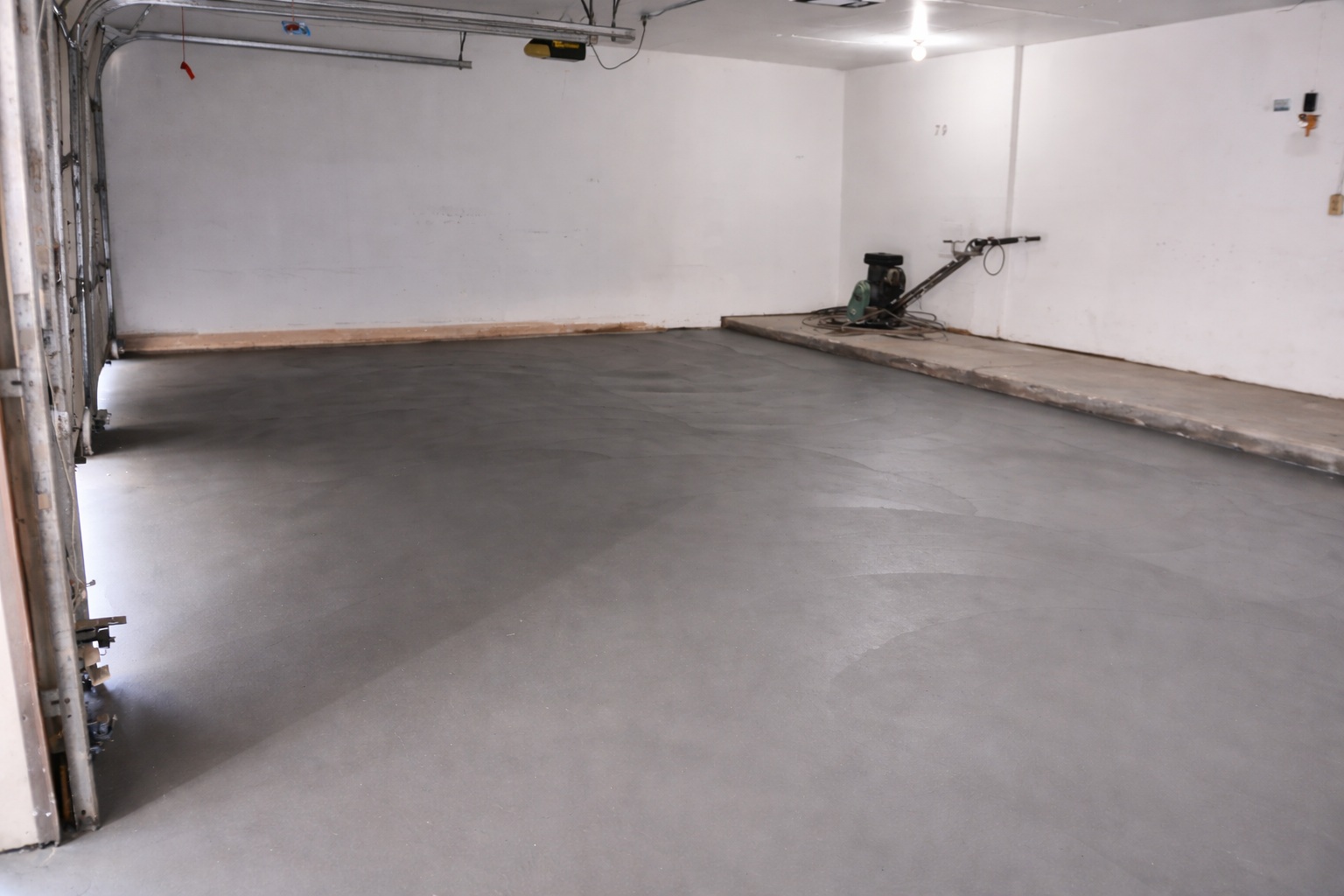 A freshly poured gray concrete floor in an empty garage, with a power trowel visible.