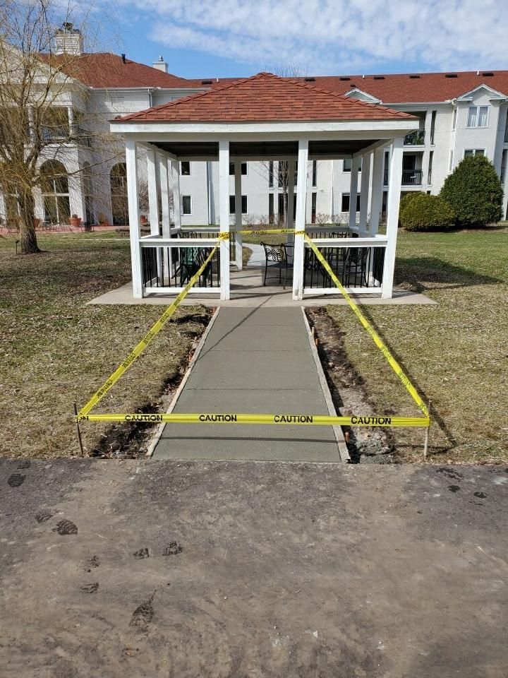 Freshly poured concrete walkway leading to a gazebo, cordoned off with yellow tape.