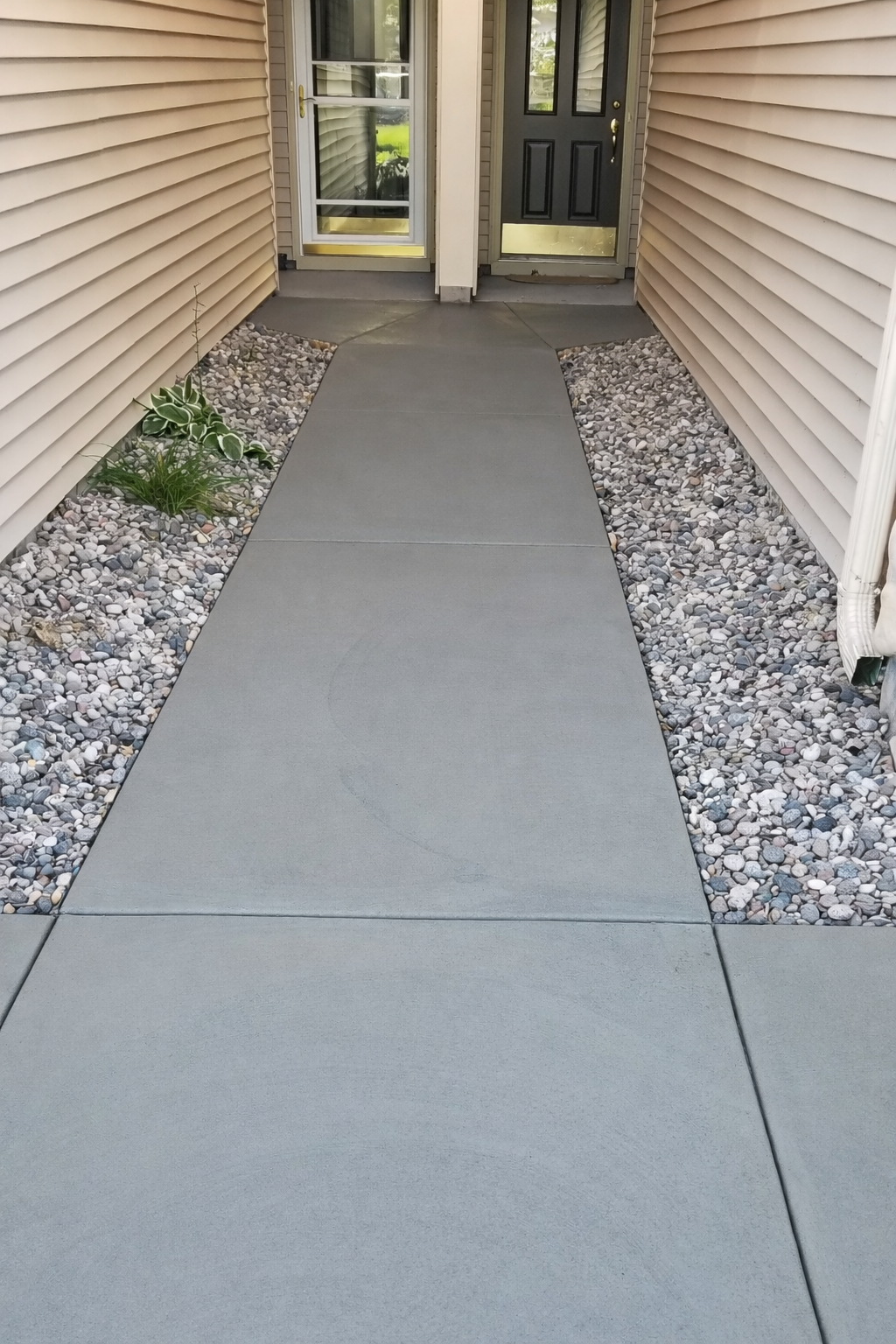 A gray concrete walkway with gravel borders leads to two doors. Light beige siding surrounds.