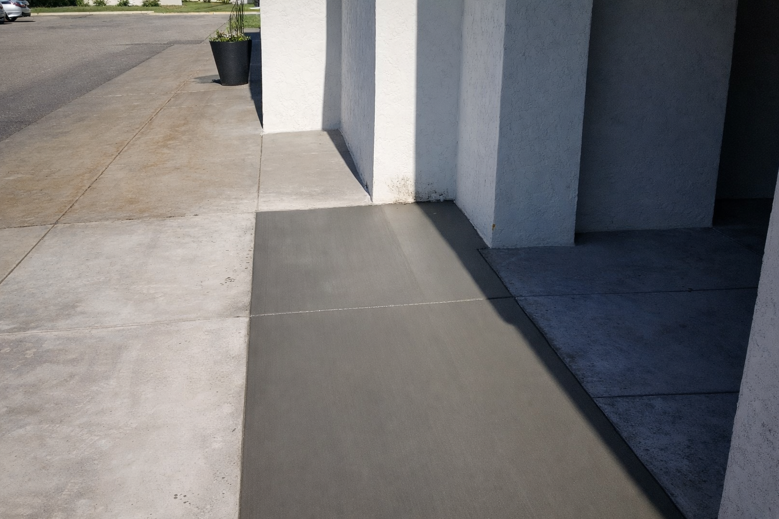 Cement walkway leading to a building with white pillars; a dark gray area under the building's overhang.