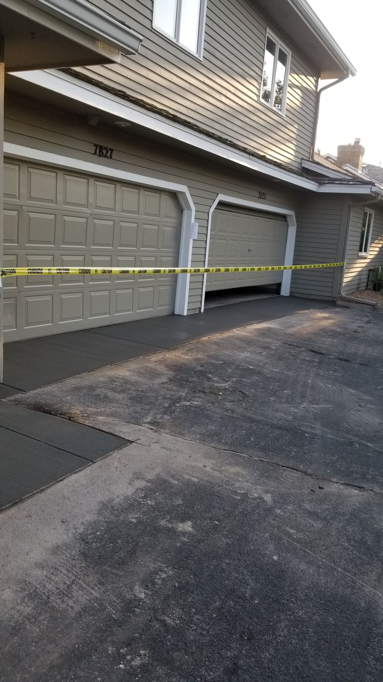 Two-car garage with one door partially open, driveway, yellow caution tape across the opening.
