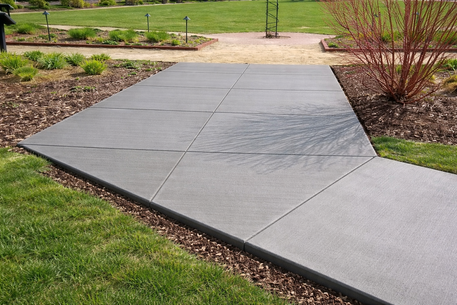 Gray concrete walkway in a garden, with grass on one side and mulch on the other.