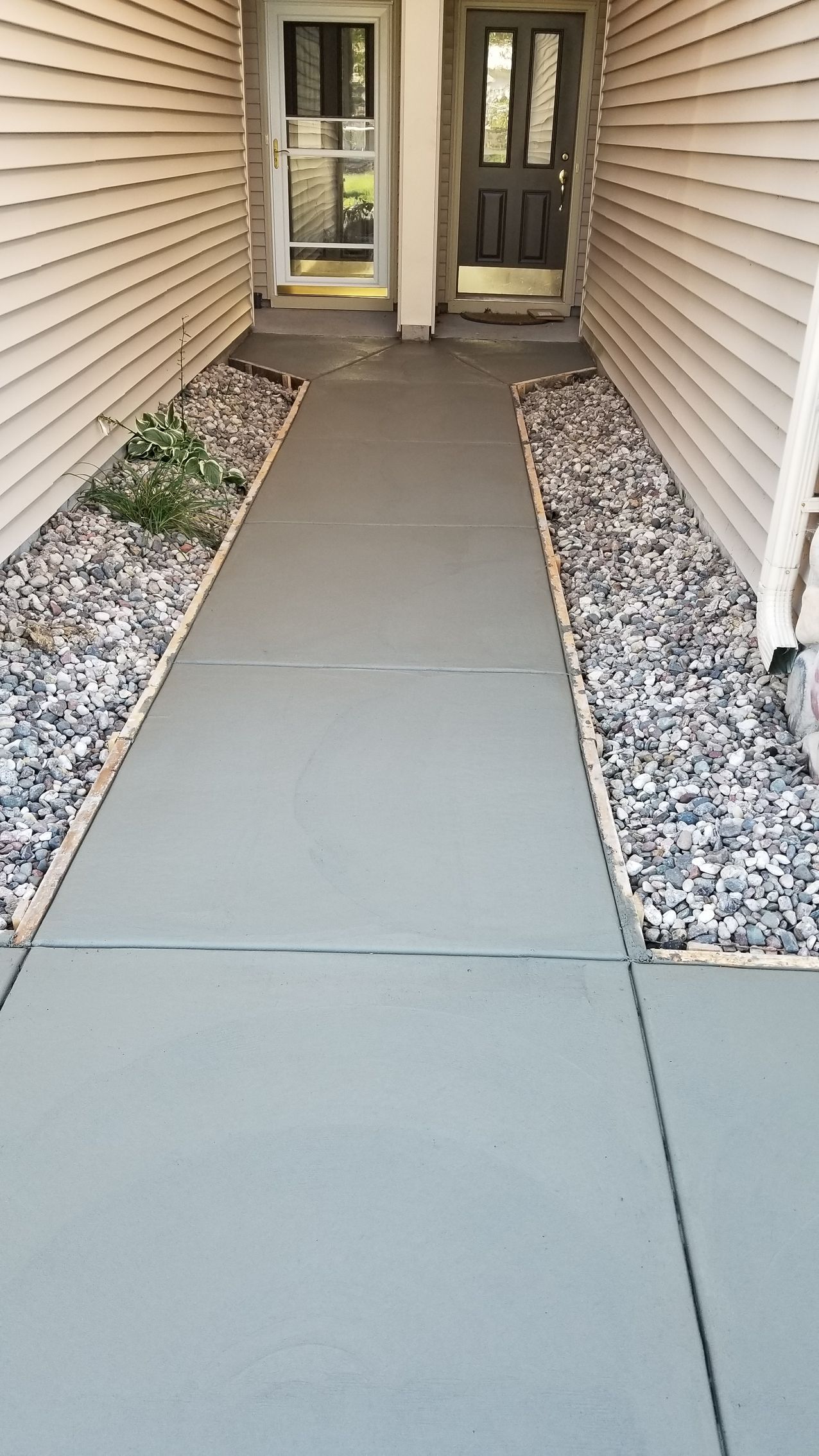 Gray concrete walkway between two buildings with rock borders.