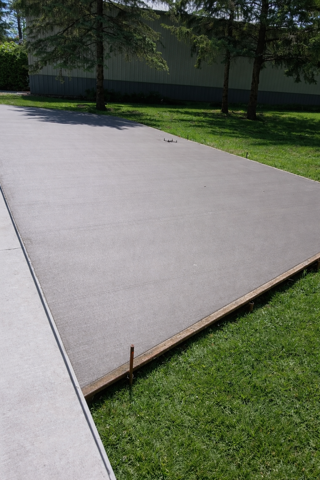 Asphalt surface bordered by wood planks and grass, with trees and building in background.