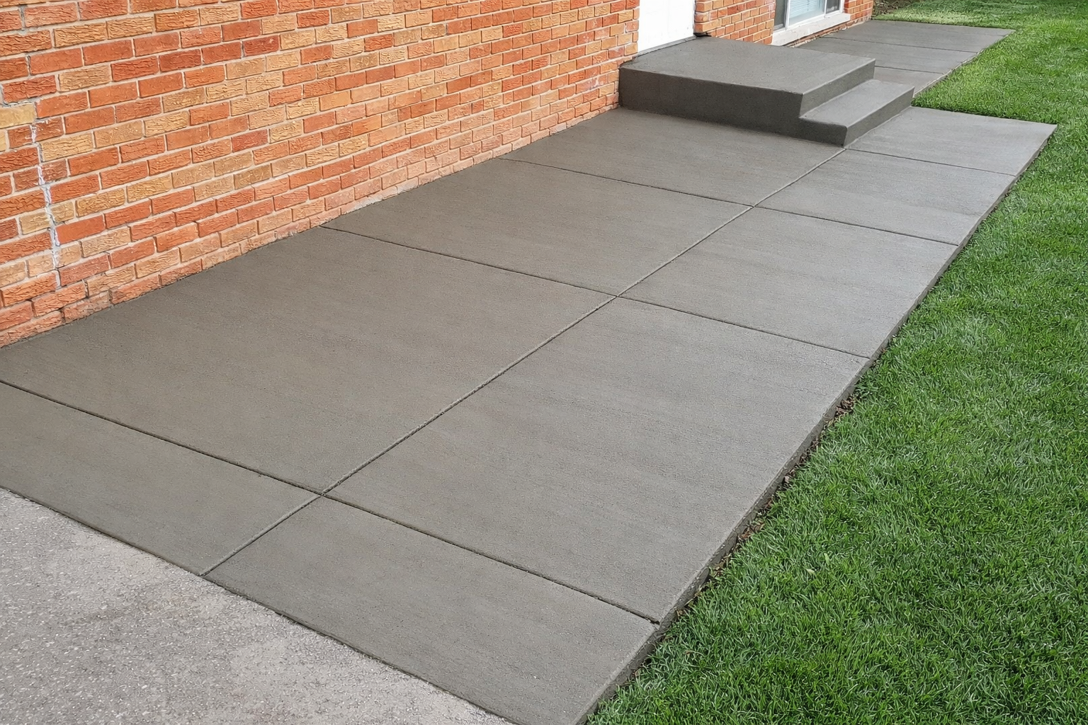 Concrete sidewalk with brick wall and green grass.
