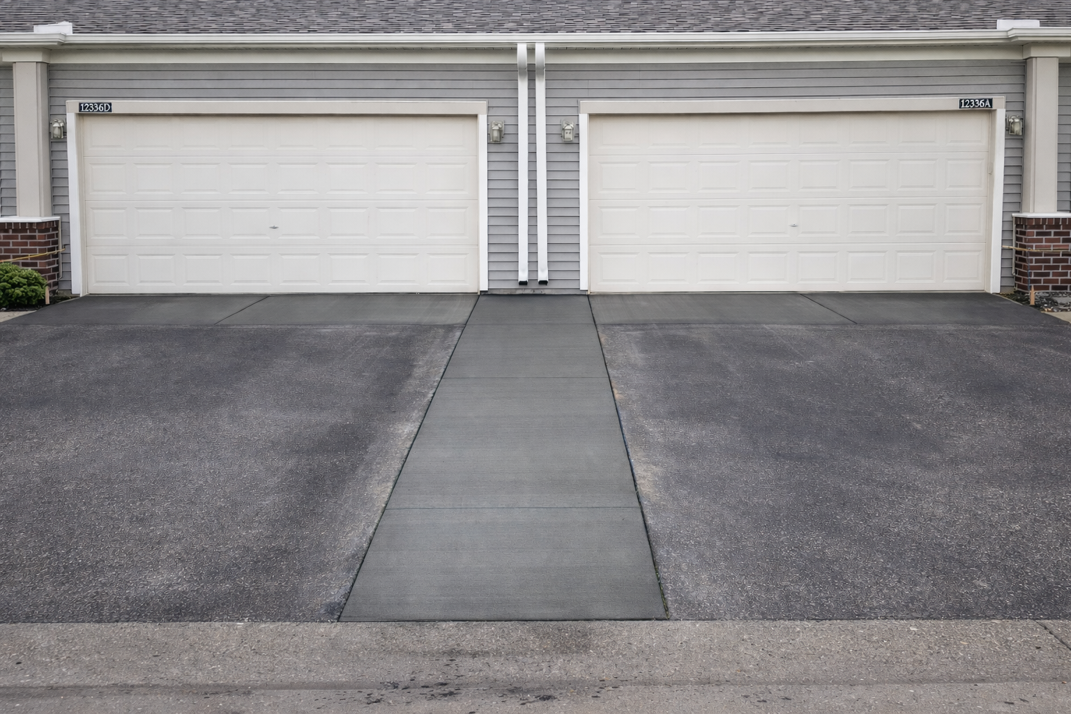 Two white garage doors with black asphalt driveways, a concrete path in between.