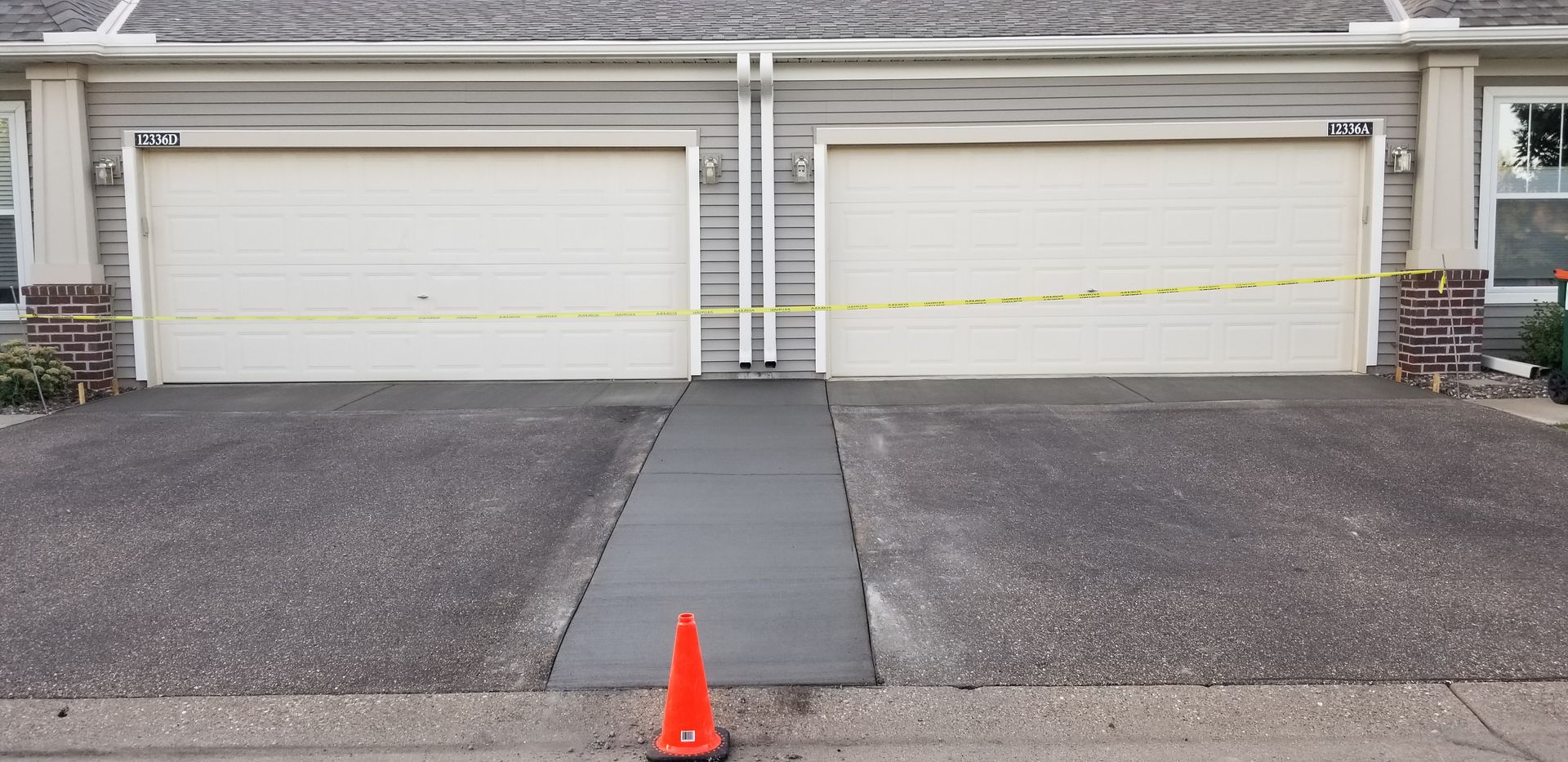 Two garage doors with caution tape and a new concrete ramp. An orange cone is in the foreground.