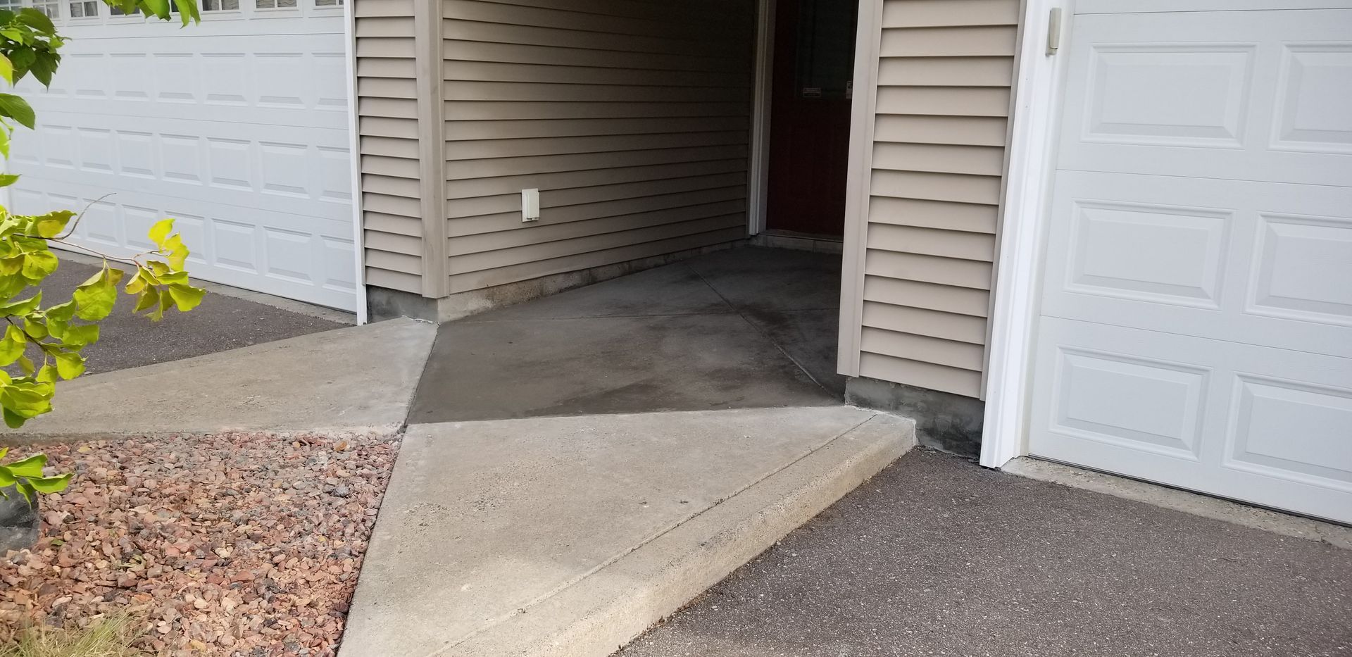 Entrance to a garage with a concrete walkway, siding, and a white garage door.