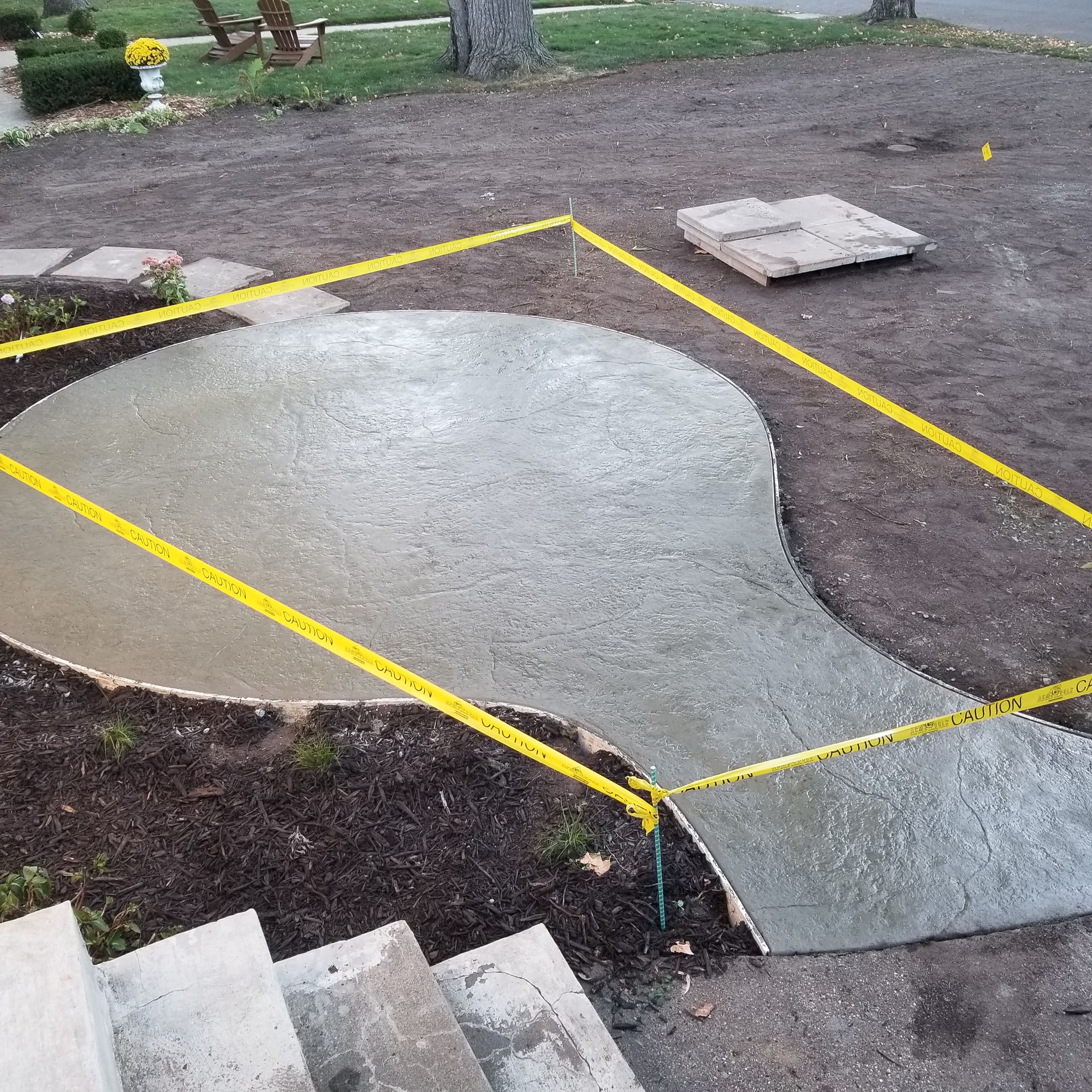 Freshly poured concrete walkway, yellow caution tape surrounds it. Stairs visible in foreground.