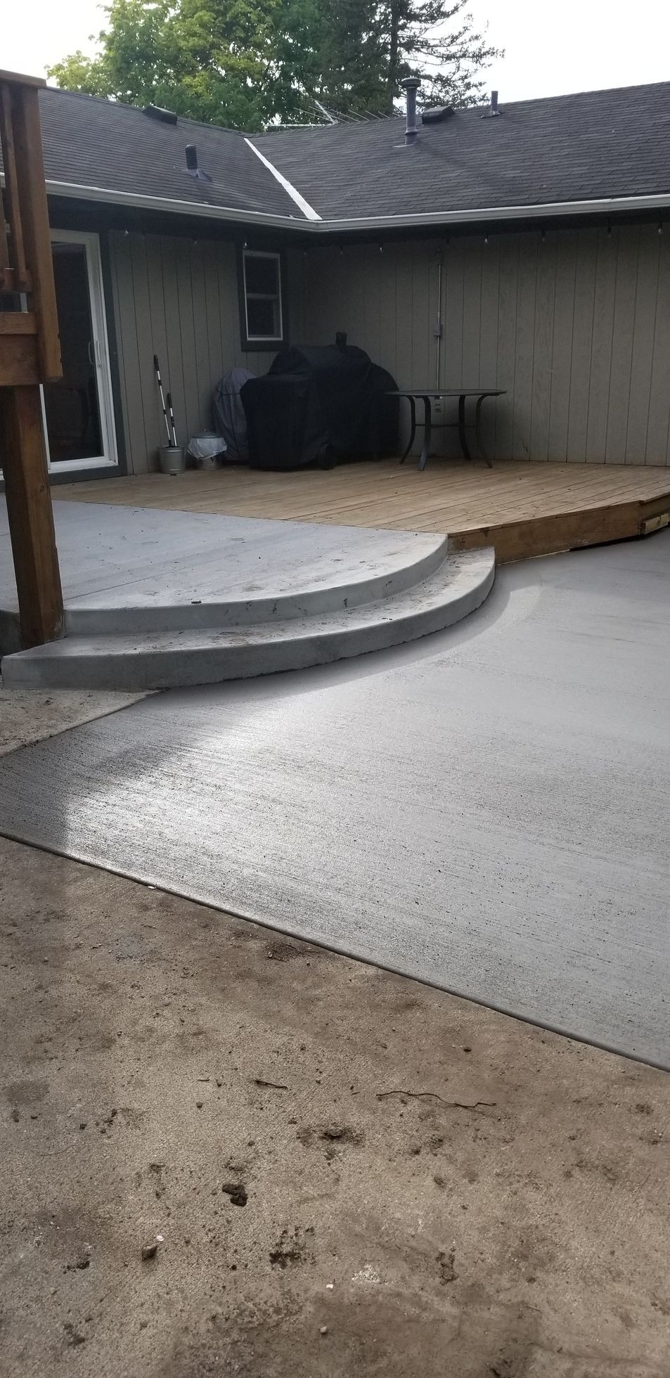 Backyard with concrete patio, steps, grill, and house.