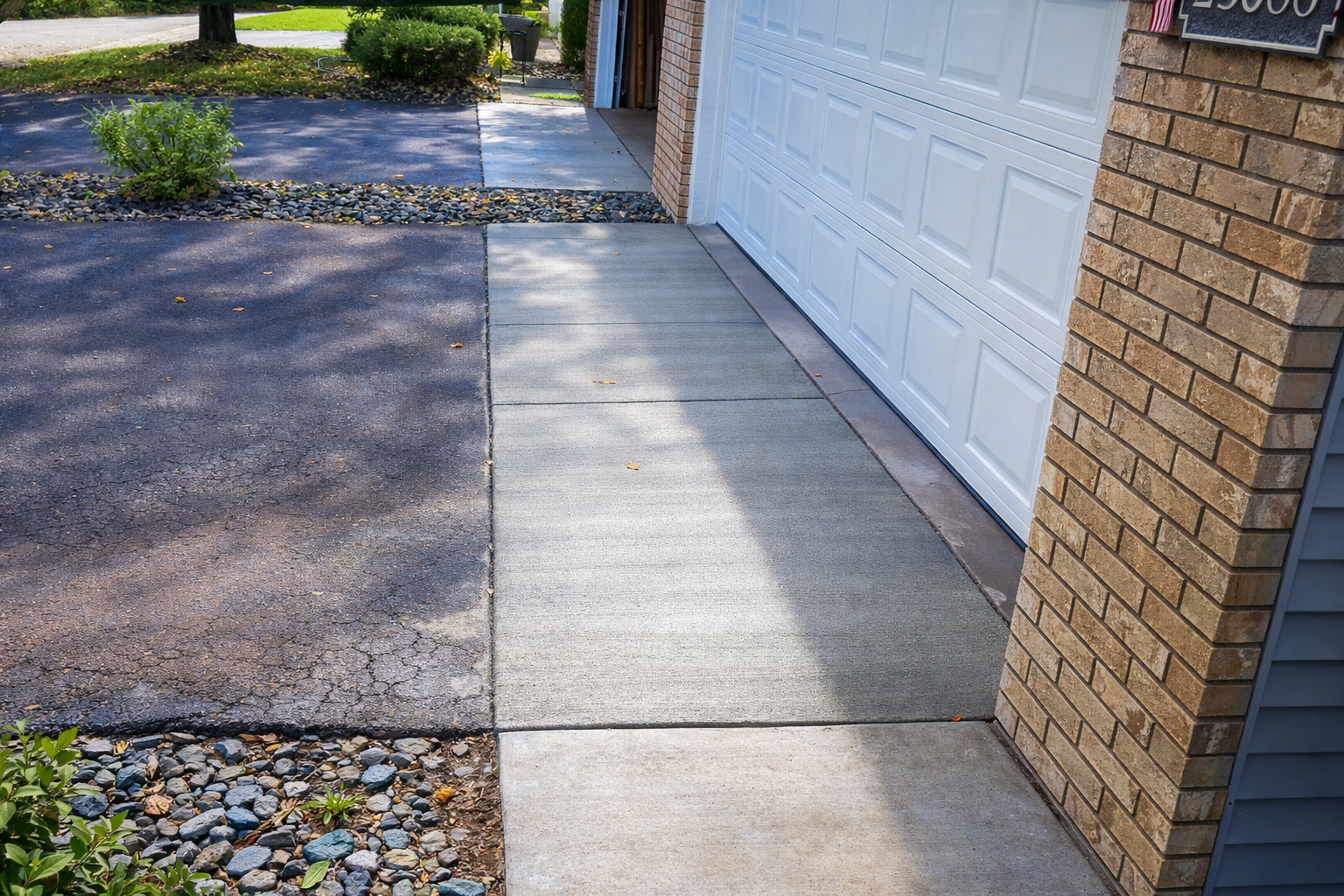Driveway and sidewalk leading to a garage. Asphalt driveway transitions to concrete sidewalk.