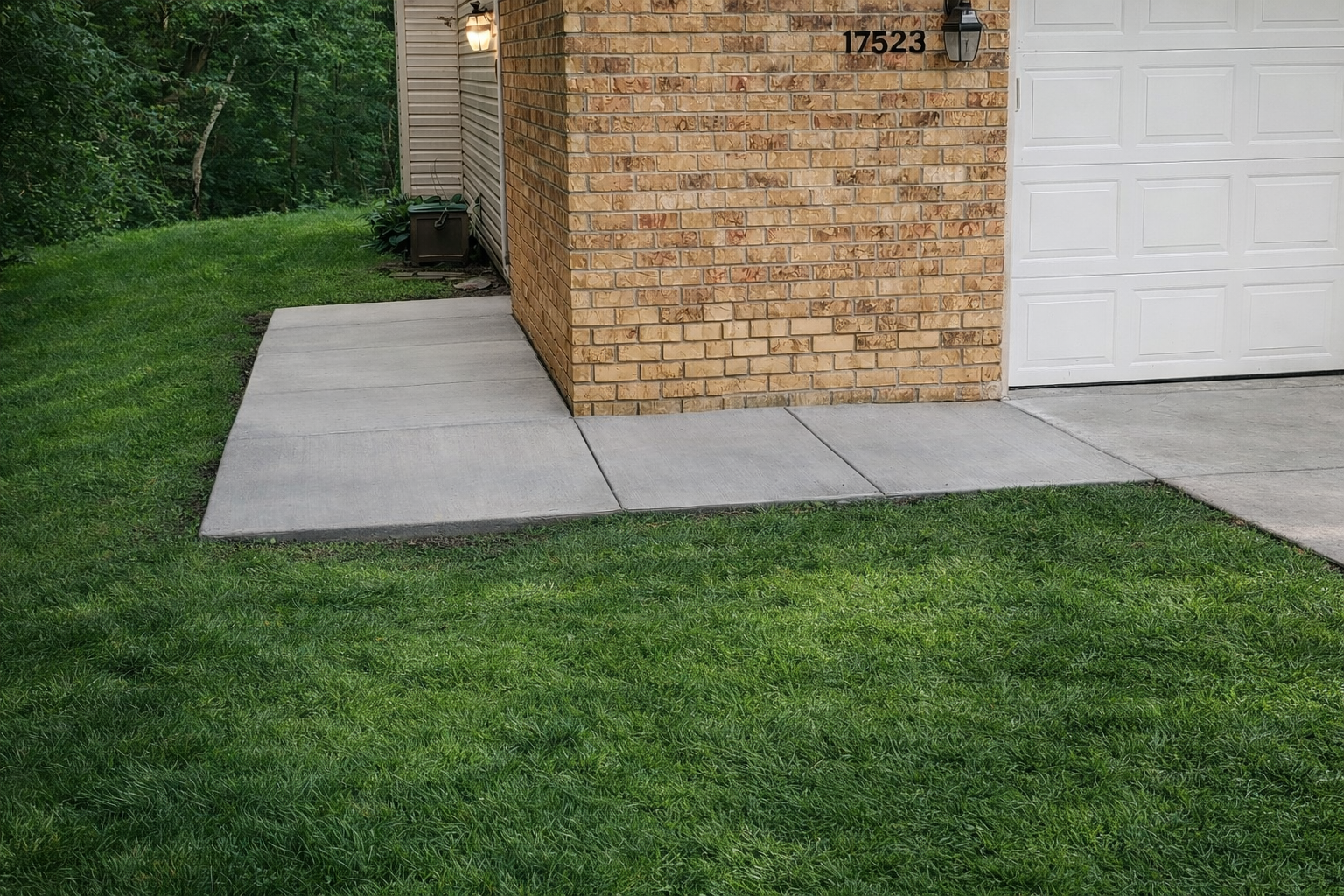 Concrete sidewalk leads to a brick wall of a building. Green grass surrounds it.