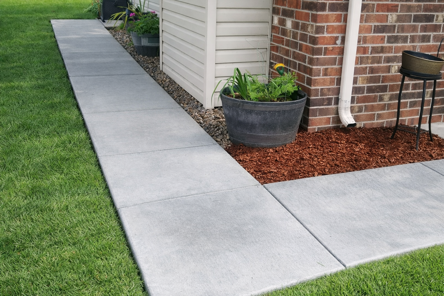 Concrete walkway next to a building and lawn, with potted plants on either side.