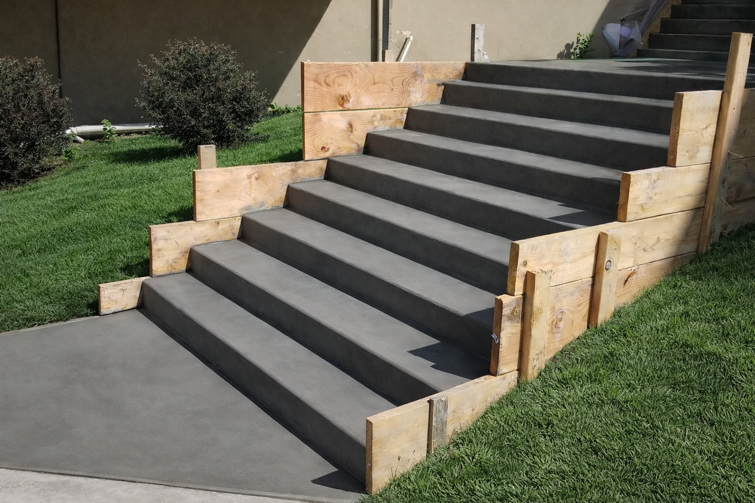 Concrete steps being constructed, framed by wood forms, in a grassy yard.