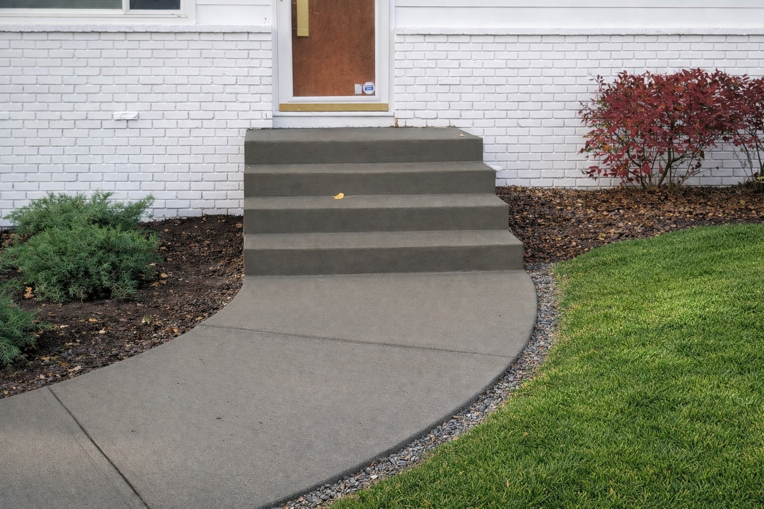 Concrete steps leading to a front door of a house with a curved sidewalk and landscaping.