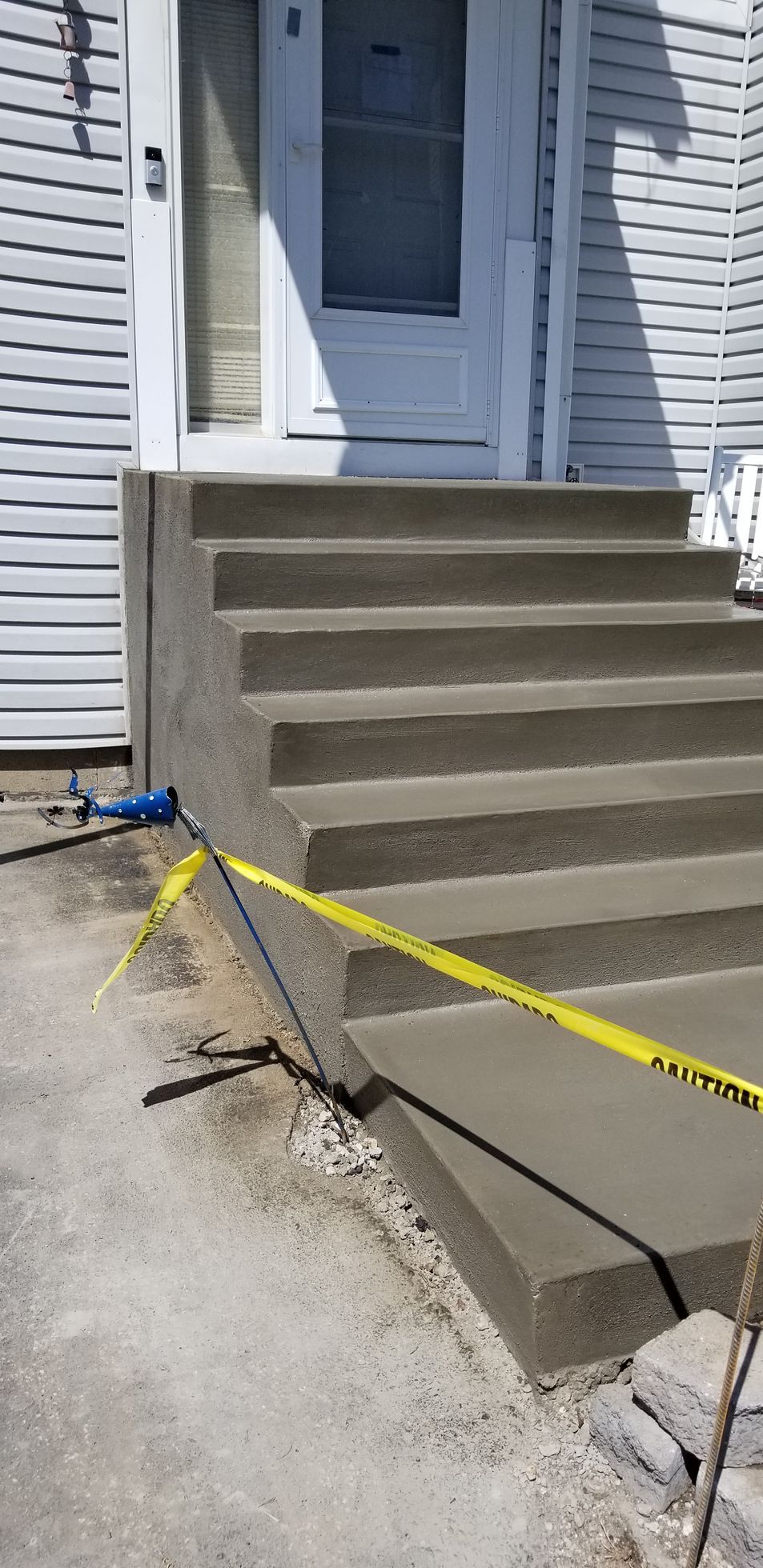 Newly poured concrete steps leading to a white door, with yellow caution tape in front.