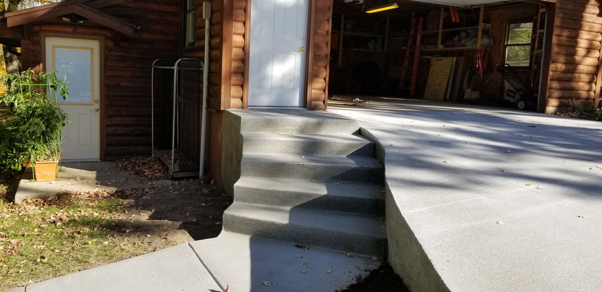 Concrete steps and ramp leading to a garage and door of a log cabin style building.
