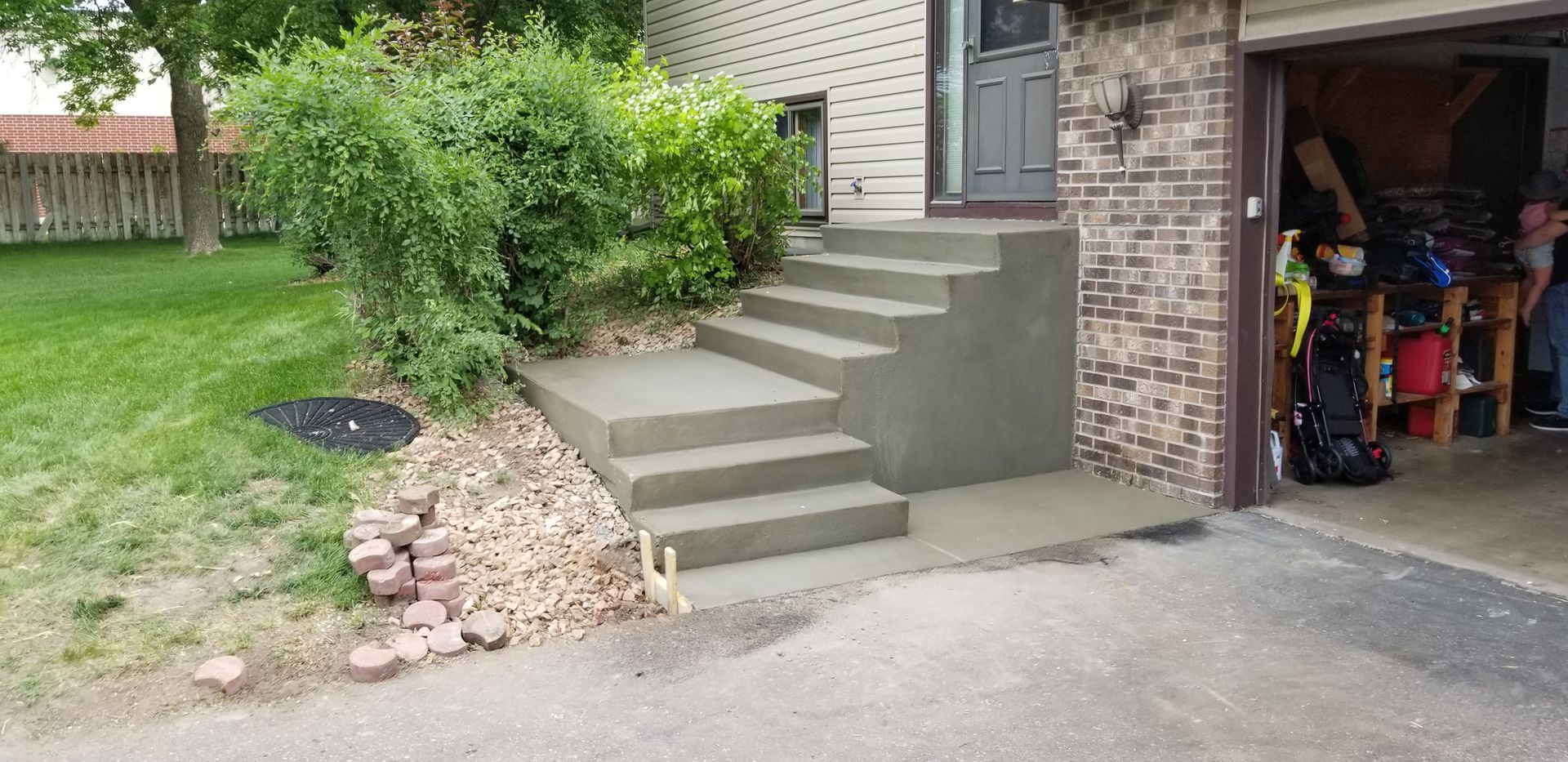 Concrete steps leading up to a gray door, next to a garage and landscaping.