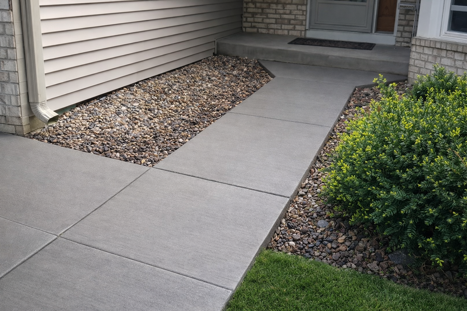 Concrete walkway leading to a front door, flanked by gravel and landscaping.