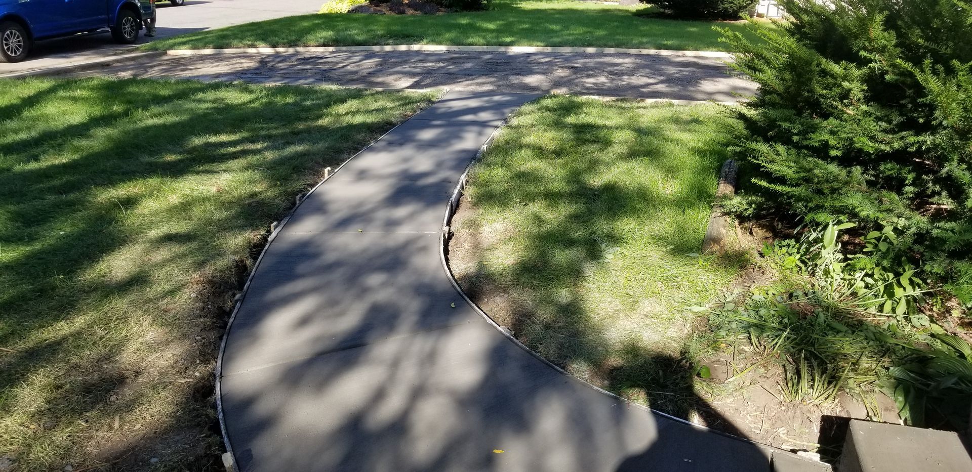 A dark gray paved path curves through green grass with a blue car in the background.