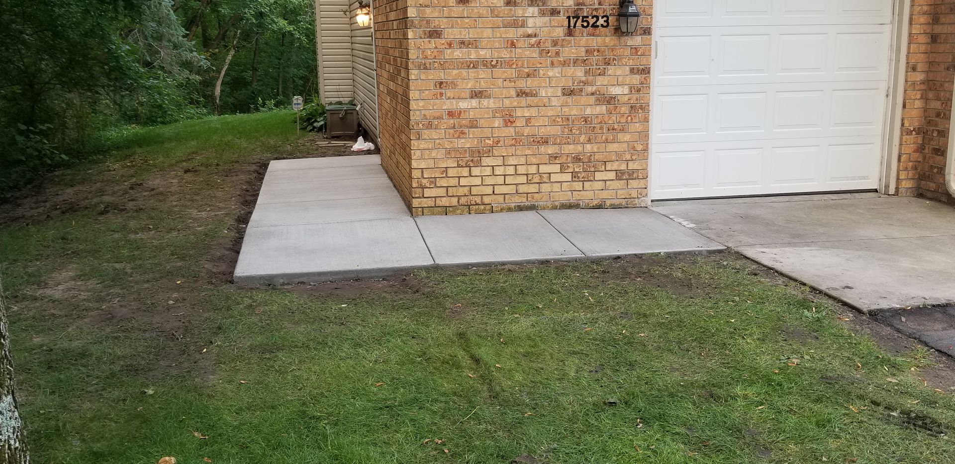Lawn with concrete walkway leading to a brick building with a garage door.