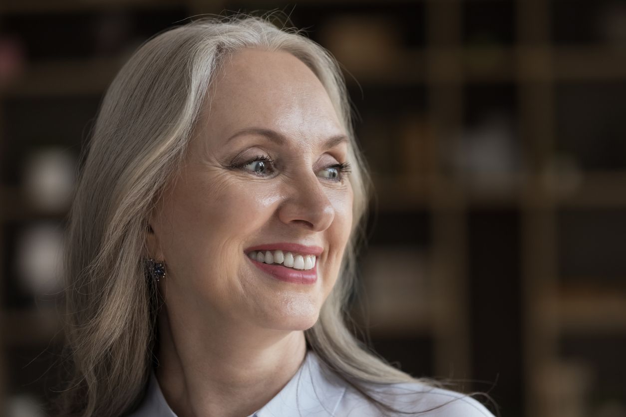 A close up of a woman with long gray hair smiling.