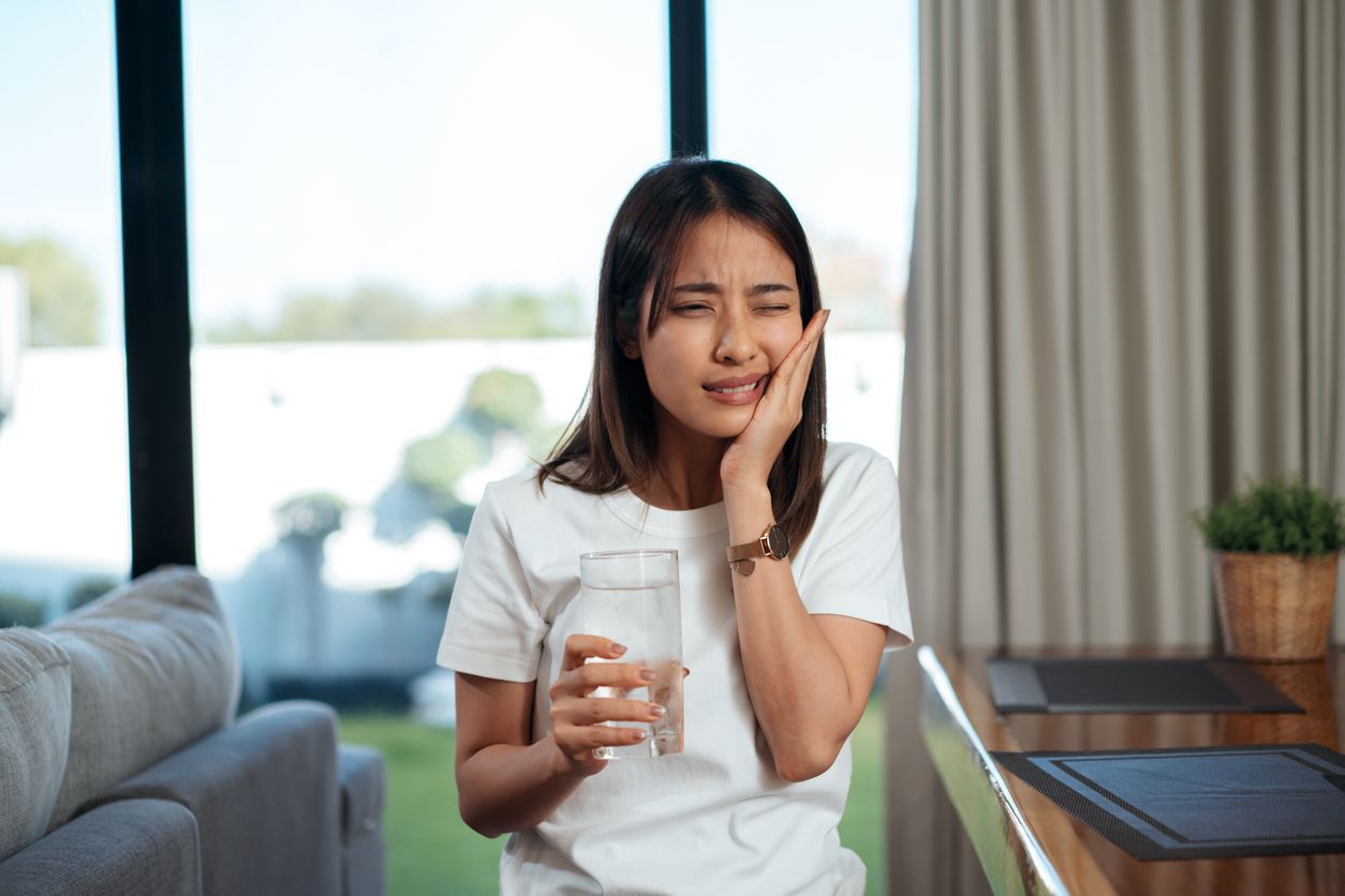 A woman is holding a glass of water and has a toothache.