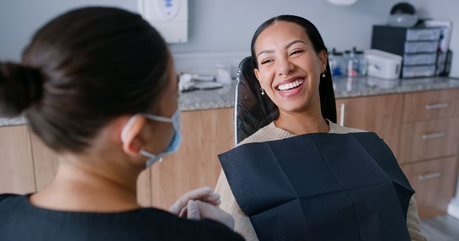 A woman is smiling while sitting in a dental chair.