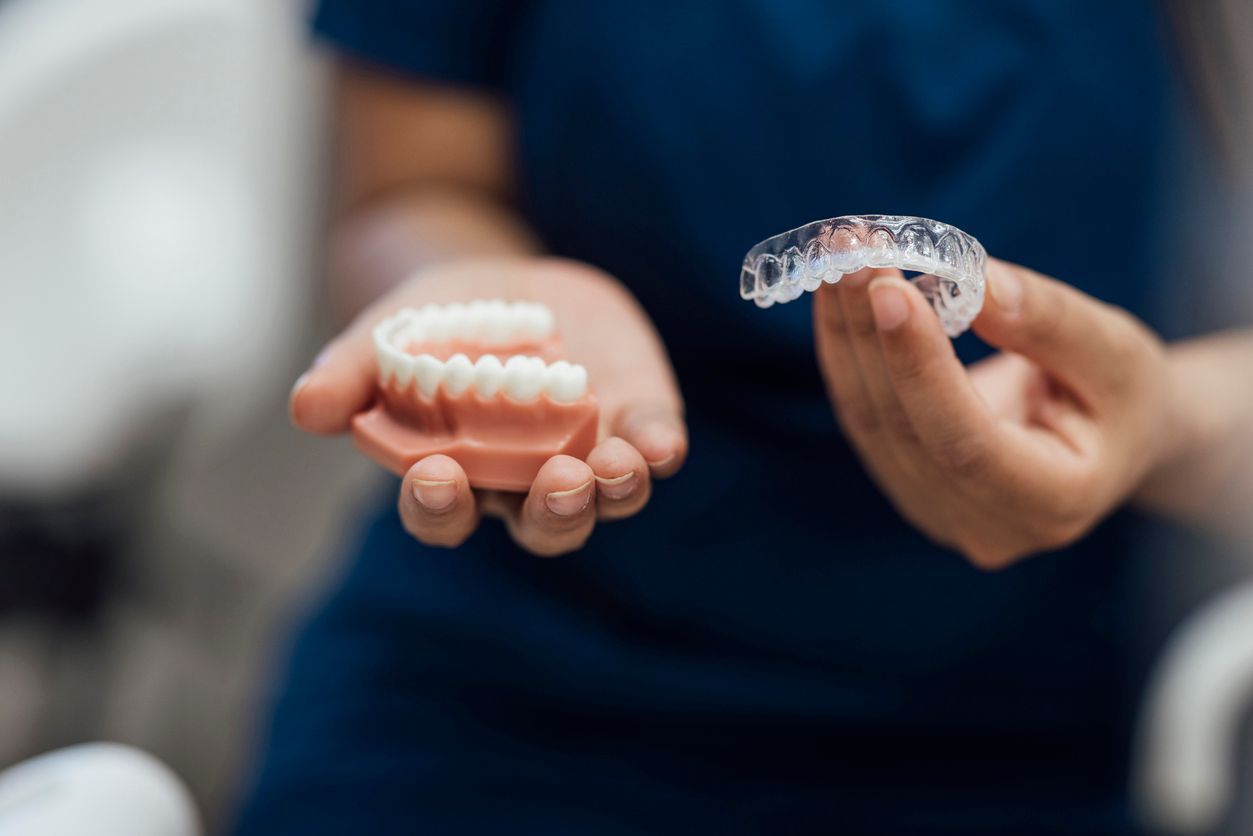 A woman with curly hair is smiling while holding a clear retainer in her hand.