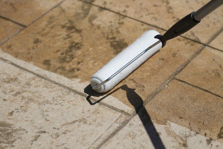 White paint roller applying sealant to tan stone patio.