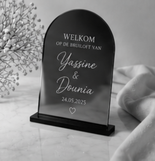 Black arched wedding sign on a stand with white text: “Welkom op de bruiloft van Yassine & Dounia” and date 24.05.2025