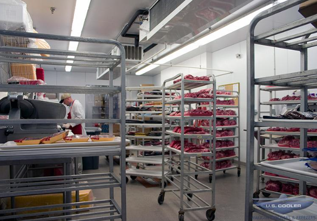 A man is working in a kitchen with a lot of shelves full of meat