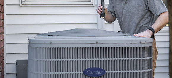 Technician working on a gray Carrier outdoor HVAC unit beside a house