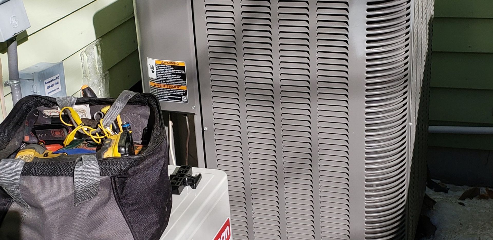 A bag filled with tools is sitting next to an air conditioner.