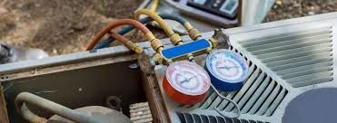 A pressure gauge manifold with red, blue, and yellow hoses connected to an outdoor air conditioning unit.