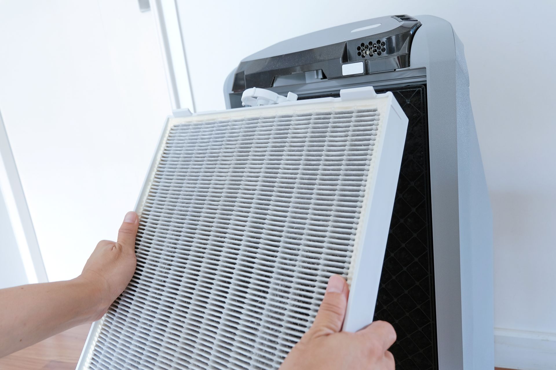 A person is holding a filter in front of an air purifier.